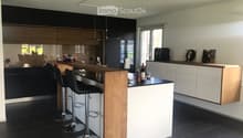 Modern kitchen with dark cabinets, wooden island, black stools, and pendant lights.