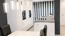 Modern kitchen and dining area with white cabinets, a central island, pendant lights, and a dining table with black chairs.