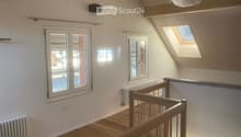 Bright hallway with wooden flooring, white walls, multiple windows including a skylight, and a wooden staircase railing.