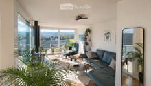 Bright living room with large windows and a view, featuring a dark blue sofa, coffee table, armchair, and decorative plants.