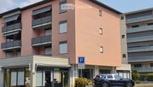 Modern multi-story residential building with pink facade, balconies, and private parking area.