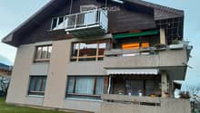 Two-story house with wooden facade, multiple balconies, large windows, and a well-maintained lawn.