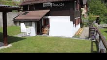 A two-story house with a red-tiled roof, white and dark wooden exterior, surrounded by a well-maintained lawn and garden area.