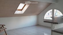 Bright, airy attic room with wooden slatted walls, skylight windows, tiled floor, and a single wooden chair near the wall.