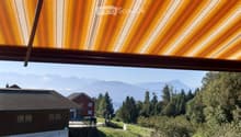 Balcony with a view of a house, trees, and mountains in the background.
