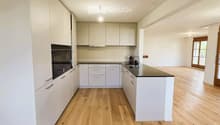 Modern kitchen with white cabinets, black countertops, and wooden floors.
