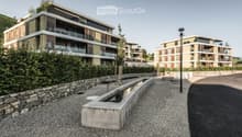 Modern multi-story residential buildings with balconies and contemporary design, surrounded by greenery and a paved walkway.