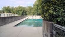 Outdoor swimming pool area with concrete walls, tiled deck, and surrounding greenery.
