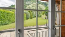 Balcony with wooden decking, metal railing, and scenic view of a green lawn, trees, and hills.