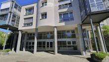 Modern building with a curved facade, large glass windows, and a raised ground floor supported by concrete pillars.
