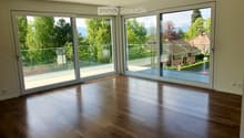 Empty room with wooden flooring and large sliding glass doors leading to a balcony with a scenic view of trees and mountains.