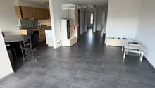 Open-plan living and dining area with grey tiled flooring, modern kitchen area with cabinets and appliances, and a dining table with chairs.