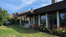 Well-maintained garden with a lawn, patio seating area, covered outdoor space, and colorful flower beds.
