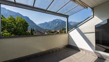 Balcony with tiled floor, glass roof, and scenic mountain view.
