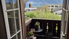 Balcony with a scenic mountain view, featuring a small round table, two flower pots, a wooden stool, and decorative vases.