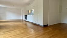 Empty room with light wooden flooring and white kitchen cabinets, no furniture or appliances present.