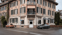 3 story brick building, large windows, awnings, balconies, cars parked in front