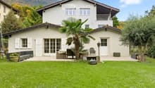 Two-story white house with a balcony, surrounded by a well-maintained lawn, palm tree, and outdoor seating area.