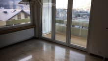 Empty room with large sliding glass doors leading to a balcony, polished stone floor, radiator, and a view of the city and mountains.