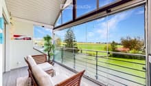 Spacious balcony with large glass windows offering a scenic countryside view, featuring a wooden sofa and a potted plant.