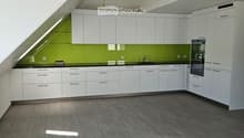 Modern kitchen with white cabinets, grey tiled floor, green backsplash, and built-in oven.