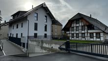 Two-story house with white exterior and multiple windows, adjacent to a traditional half-timbered house with a sloped roof.