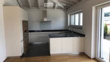 Modern kitchen with white cabinets, black countertops, and a wooden accent wall. Features a sink, faucet, and an oven.