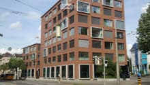 modern multi-story building, brick facade, glass windows, balconies, ground-level storefronts, overhead power lines