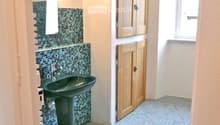 Bathroom with a dark green sink, matching faucet, and wooden cabinets. The walls and floor are tiled in blue and grey.