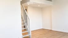 Empty room with light wooden flooring and white walls, featuring a white staircase leading to an upper level.