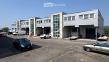 Modern industrial building with large garage doors, multiple windows, and a spacious parking lot with several cars.