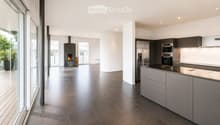 Modern kitchen with stainless steel appliances, dark grey cabinets, and a central island. Features a fireplace and large windows with a view of greenery.