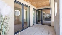 Modern balcony with large glass sliding doors, wooden ceiling, tiled floor, and circular mirrors on walls.