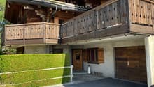 A two-story wooden house with a balcony, garage, and well-maintained garden.