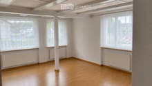 Empty room with wooden flooring, white walls, large windows with sheer curtains, radiators, and exposed ceiling beams.