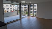 Empty room with wooden flooring and large glass sliding doors leading to a balcony. The balcony has a tiled floor and metal railing.