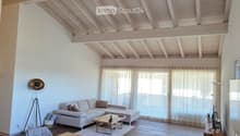 Open-concept living and dining area with exposed wooden beams, white sofa, coffee table, dining table, and chairs.