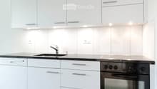 Modern kitchen with white cabinets, black countertop, stainless steel sink, and built-in oven and dishwasher.