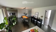 Modern open-plan living and dining area with a sofa, coffee table, dining table, chairs, cabinet, lamp, plant, and picture frame.