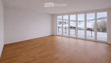 Empty room with wooden flooring and large sliding glass doors leading to a balcony with a view of a snowy landscape.