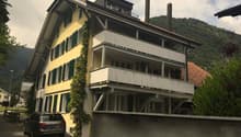 3-story yellow house, green shutters, brick chimneys, balcony on second floor, car parked in front