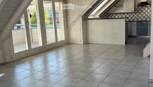 Bright, airy attic space with wooden beams, large skylights, and a modern kitchen area featuring light-colored cabinets and a dishwasher. The floor is tiled, and there is a sliding glass door leading to an outdoor area.