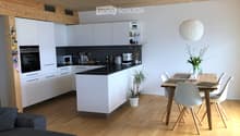 Modern kitchen and dining area with white cabinets, black countertops, a central island, a dining table with chairs, and a pendant light.
