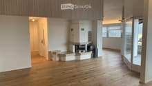 Empty room with wooden flooring, white walls, and a fireplace with a stone surround. The room has large windows and a glass door leading to another space.