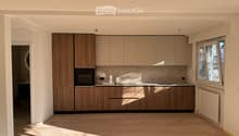 Modern kitchen with light wood cabinets, stainless steel oven, and wooden flooring.
