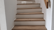 A modern staircase with wooden steps and a matching wooden handrail, set against white walls.