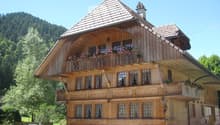 Traditional wooden house with a steep roof, multiple windows, and flower boxes on the balcony and ground level.