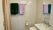 Modern bathroom with white tiled walls, dark grey tiled floor, toilet, sink, mirror, and towels.