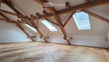 Empty attic space with exposed wooden beams, light-colored wooden flooring, and skylight windows allowing natural light.