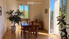 Bright dining area with wooden floor, large windows, dining table with chairs, potted plants, and a cabinet.